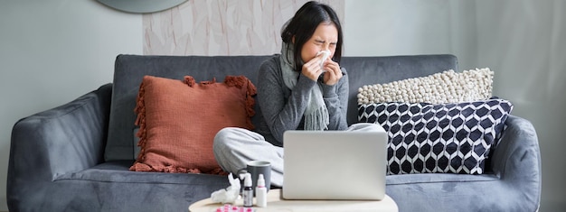 Free Photo young asian woman staying at home feeling unwell catching a cold sick leave sitting with laptop