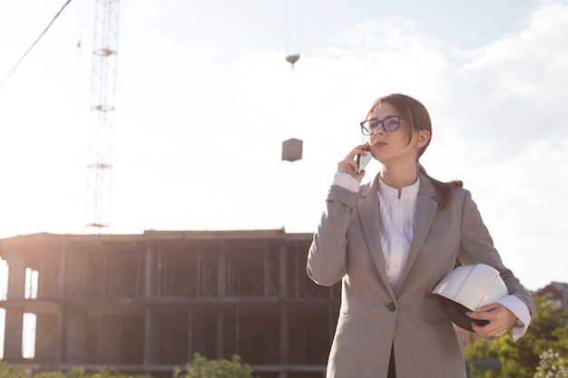 Young attractive female architect talking on cellphone at construction site