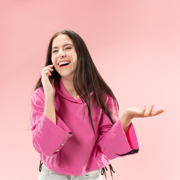 Young beautiful woman using mobile phone studio on pink color studio background. Human facial emotions concept. Trendy colors