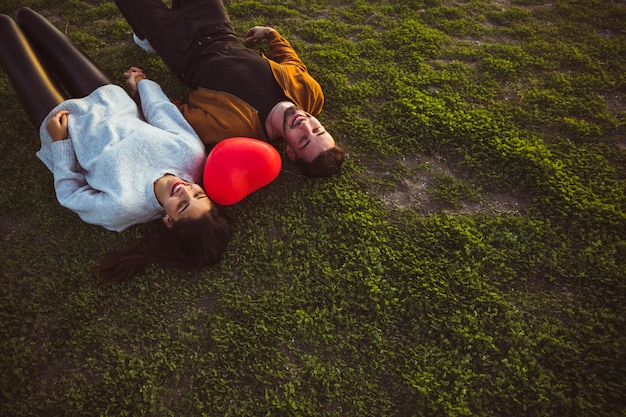 Foto gratuita giovane coppia sdraiata sull'erba con palloncino cuore rosso