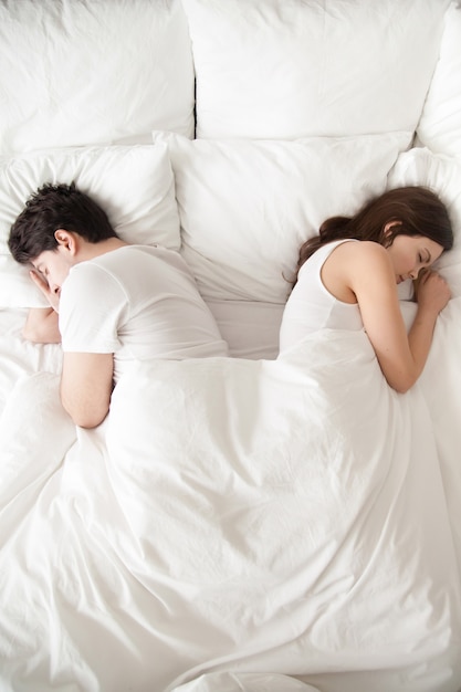 Free photo young couple sleeping separately in bed, back to back, vertical