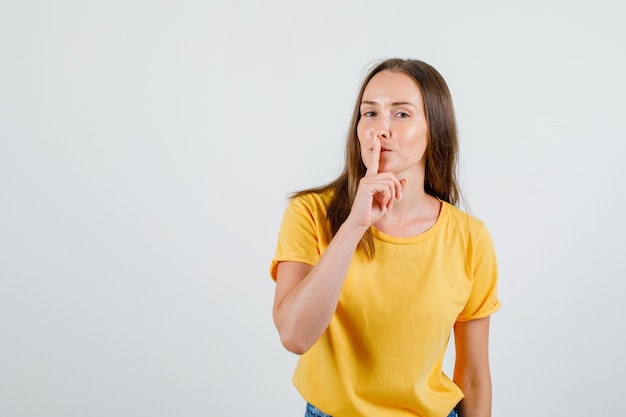 Free photo young female showing silence gesture and smiling in t-shirt, shorts front view.