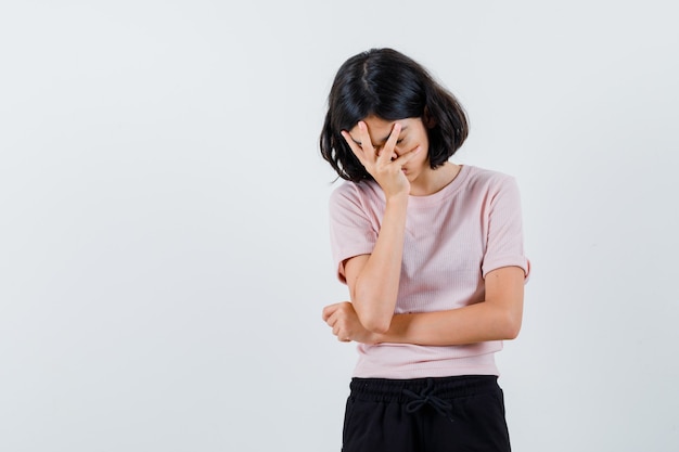 Foto gratuita giovane ragazza in maglietta rosa e pantaloni neri che copre il viso con la mano e sembra esausta