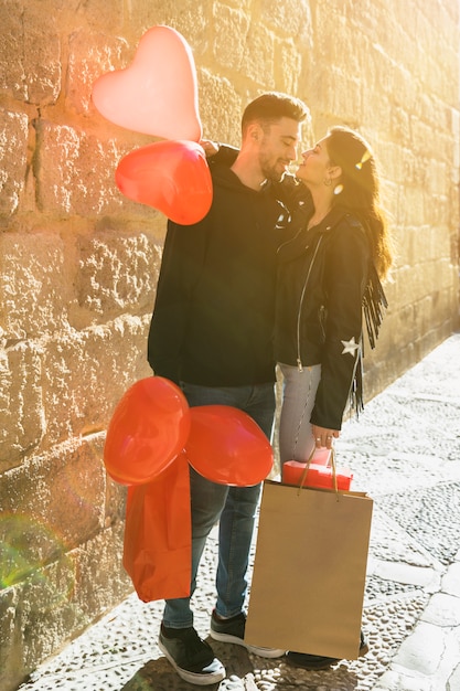 Free photo young guy with packets hugging lady with balloons on street