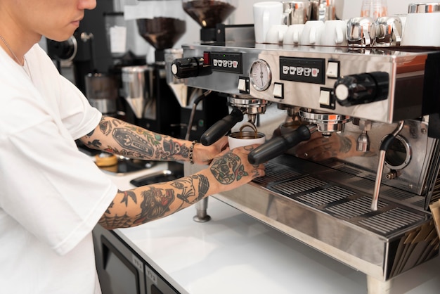 Young male barista with tattoos using the coffee machine at work