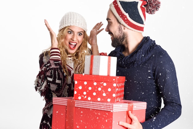 Free photo young man giving many christmas gifts to his woman, dresses with winter clothes on white background