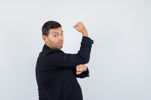 Young man showing muscles of arm in black jacket and looking powerful .