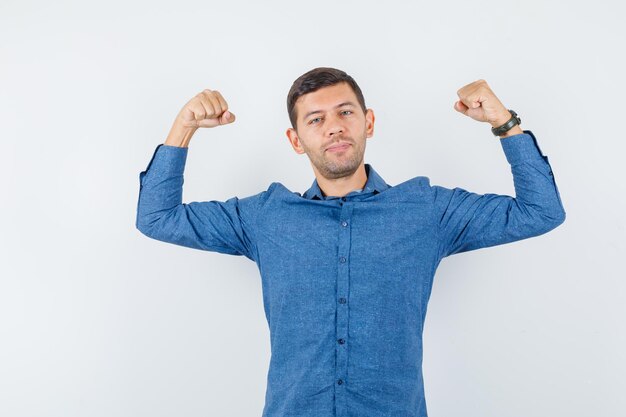 Young man showing muscles of arms in blue shirt and looking powerful. front view.