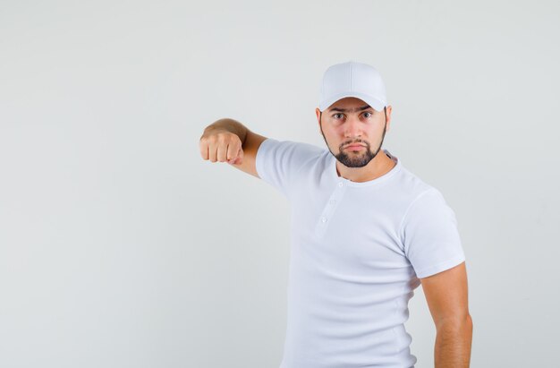 Young man in t-shirt,cap pointing at camera and looking angry , front view.