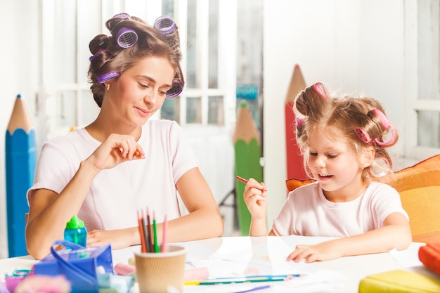 The young mother and her little daughter drawing with pencils at home