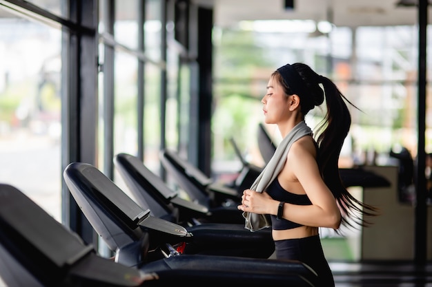 Free photo young sexy woman wearing sportswear, sweat-proof fabric and smartwatch  running on treadmill to workout in modern gym, smile , copy space