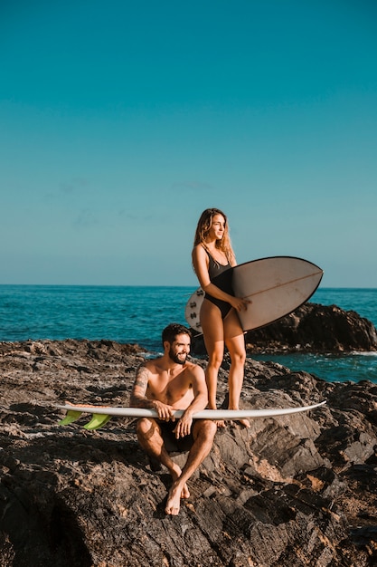 Foto gratuita giovane sorridente uomo e donna con tavole da surf sulla roccia vicino al mare