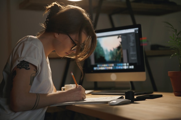 Free Photo young woman designer sitting indoors at night drawing sketches