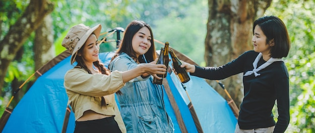 Free Photo young woman and girl friends travelers relaxing in camp chairs at tent they are cheering and drinking beer during camping talking with fun and happy together