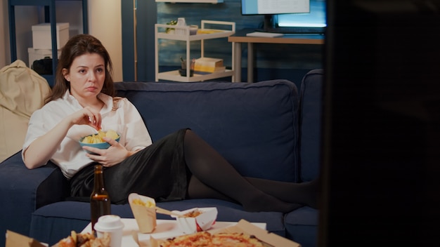 Young woman laying on couch holding bowl of chips