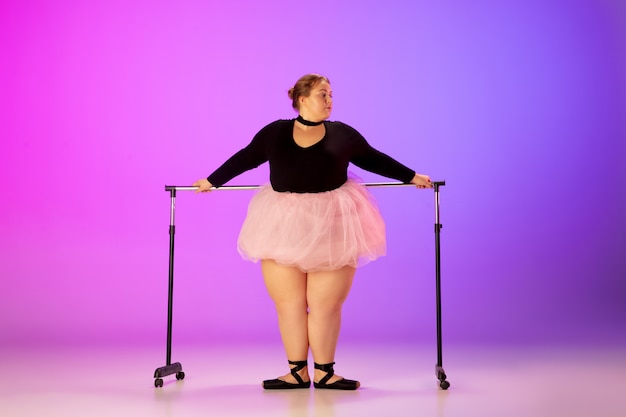 Photo gratuite beau modèle de taille plus caucasien pratiquant la danse de ballet sur fond de studio dégradé violet-rose en néon. concept de motivation, d'inclusion, de rêves et de réalisations. ça vaut le coup d'être ballerine.