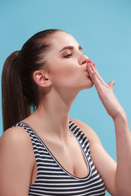 Photo gratuite beau portrait de trois quarts féminin. isolé sur fond de studio bleu. la belle jeune femme émotive est debout. les émotions humaines, le concept d'expression faciale. vue de profil. couleurs tendance