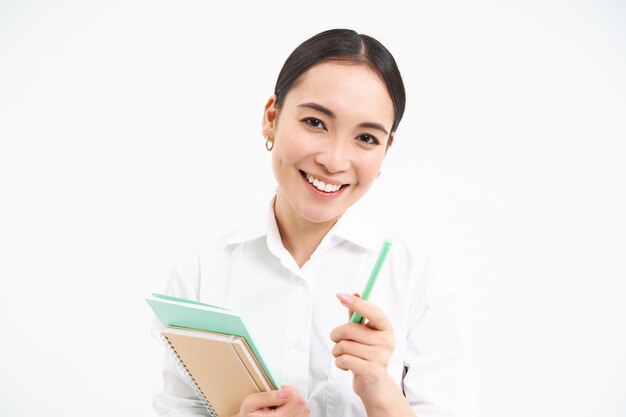 Photo gratuit belle étudiante coréenne confiante avec un stylo et des cahiers souriant et regardant heureux debout o