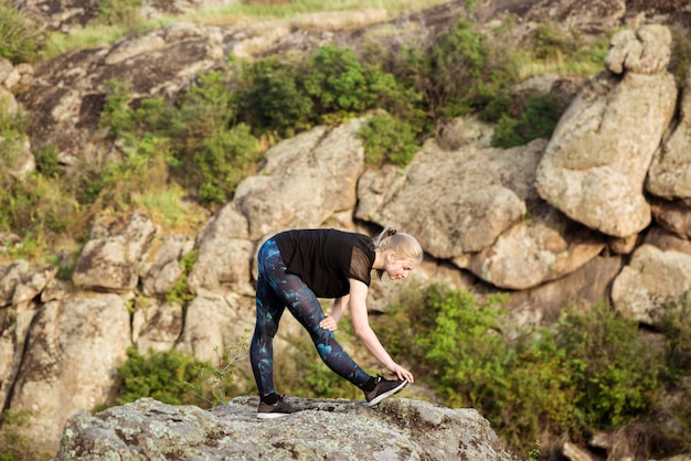 Photo gratuite belle femme blonde sportive formation, qui s'étend sur rocher dans le canyon