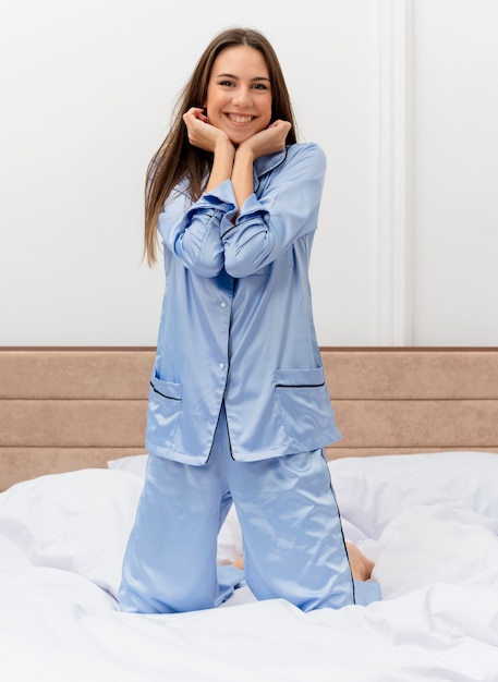 Photo gratuite belle jeune femme en pyjama bleu assis sur le lit au repos profitant du week-end heureux et positif souriant joyeusement à l'intérieur de la chambre