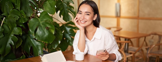 Photo gratuite belle jeune femme avec un smartphone, buvant du café au café et souriante, relaxante avec son favori