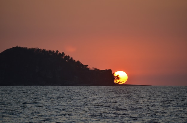 Photo gratuite belle silhouette large tourné d'un îlot couvert d'arbres par la mer sous le ciel pendant le coucher du soleil