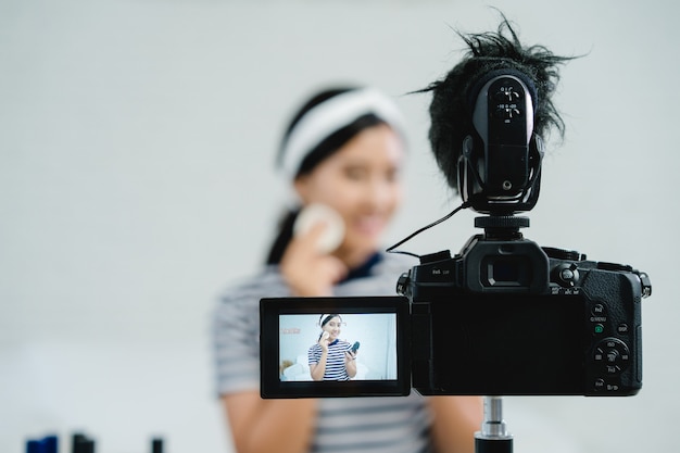 Photo gratuite une blogueuse beauté présente des produits cosmétiques en position assise devant la caméra pour enregistrer une vidéo