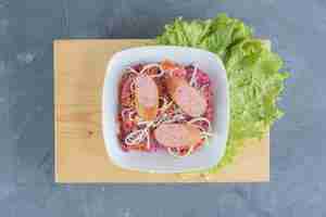 Photo gratuite bol à salade de noix et de betteraves sur une planche de bois avec des feuilles de laitue, garni de saucisses et de fromage sur une table en marbre.