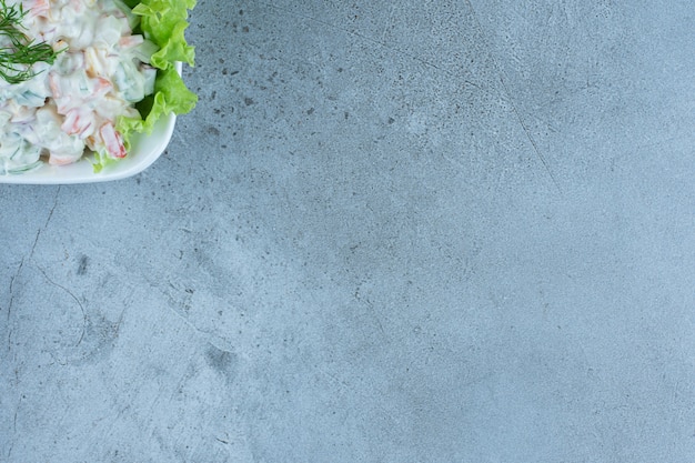 Photo gratuite bol de salade d'olivier avec une feuille de laitue sur marbre.