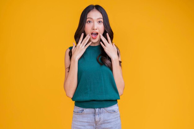 Bonheur décontracté femme asiatique souriante joyeuse en t-shirt vert bleu jean se détendre paisible pensée positive mode de vie insouciant debout geste de la main expression du visage avec un fond de couleur jaune