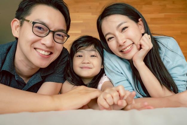 Bonheur joyeuse famille asiatique maman papa fille allongée avec amusement jouer baiser sur le lit portrait de famille asiatique personnes fond à la maison