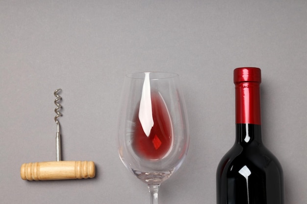 Photo gratuite une bouteille de vin, un verre et un tire-bouchon sur un fond gris.