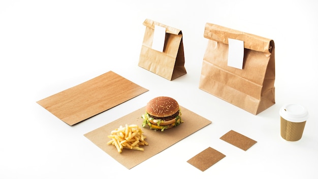 Photo gratuite burger et frites sur papier avec boisson jetable et paquet de papier sur fond blanc