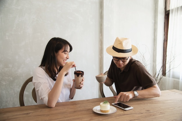 Casual homme et femme parlant joyeusement tout en buvant un café et en regardant un téléphone portable