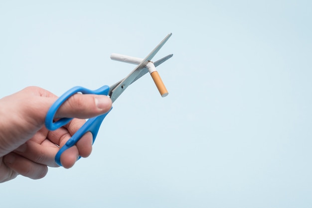 Photo gratuite cigarette avec des ciseaux sur fond bleu