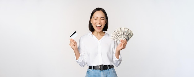 Photo gratuit concept de finances et d'argent heureuse jeune femme asiatique dansant avec de l'argent et une carte de crédit souriant heureux