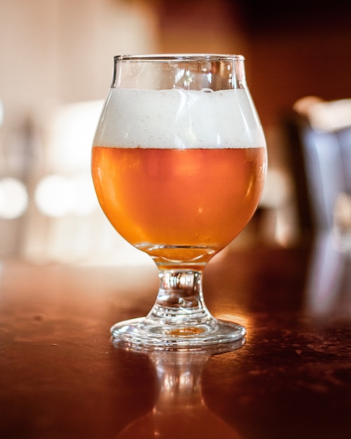 Photo gratuite coup vertical de bière dans une tasse en verre avec un arrière-plan flou