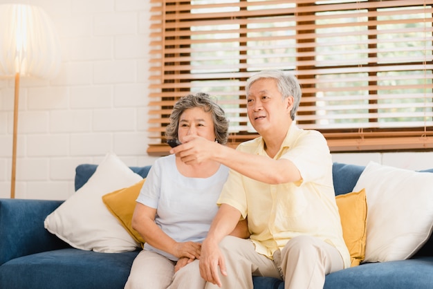 Photo gratuite couple de personnes âgées asiatique en regardant la télévision dans le salon à la maison, doux couple, profitez d'un moment d'amour en position couchée sur le canapé, détendu à la maison