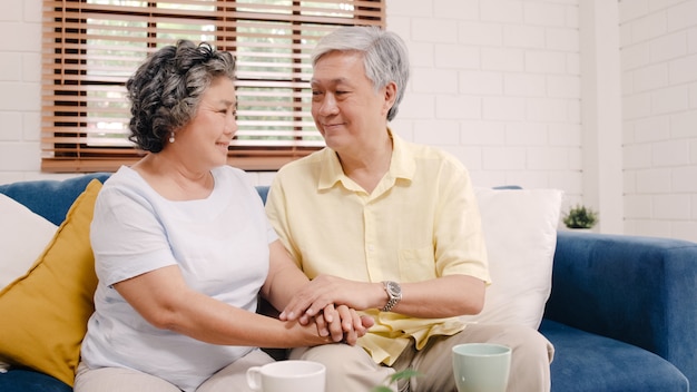 Photo gratuite couple de personnes âgées asiatique tenant leurs mains tout en prenant ensemble dans le salon, un couple se sentant heureux de partager et se soutenir mutuellement allongé sur un canapé à la maison.