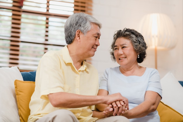 Photo gratuite couple de personnes âgées asiatique tenant leurs mains tout en prenant ensemble dans le salon, un couple se sentant heureux de partager et se soutenir mutuellement allongé sur un canapé à la maison.