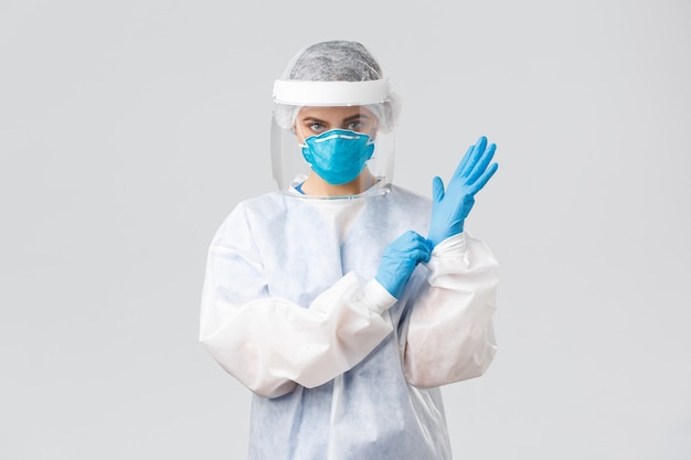 Photo gratuite covid-19, prévention des virus, santé, travailleurs de la santé et concept de quarantaine. femme médecin sérieuse en équipement de protection individuelle epi, bouclier, masque facial sur des gants pour entrer dans la chambre du patient