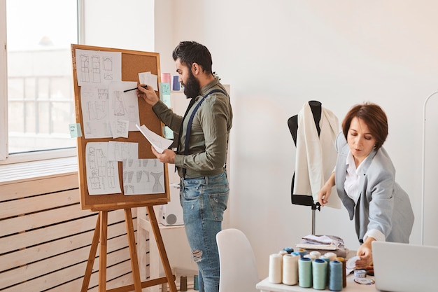 Photo gratuit créateurs de mode en atelier avec forme de robe et tableau d'idées