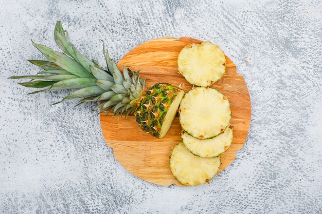 Photo gratuite délicieuses tranches d'ananas dans une planche à découper ronde sur la surface grunge, vue de dessus.