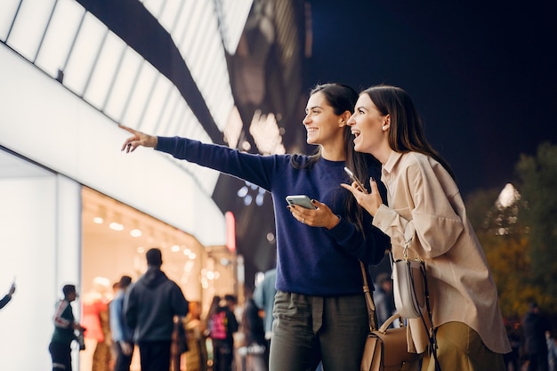 Photo gratuite deux copines utilisent leur téléphone portable tout en explorant une nouvelle ville la nuit