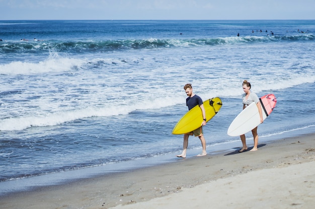 Photo gratuit deux surfeurs marchant le long du rivage