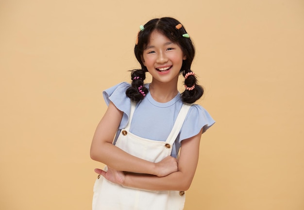 Photo gratuite des enfants asiatiques heureux, une fille positive, riant, croisant les bras, isolée sur un fond de couleur nu.