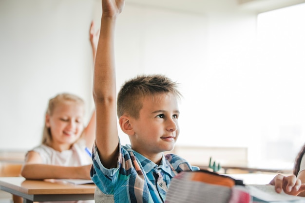 Photo gratuite enfants assis dans les bureaux de l'école en train de lever les mains