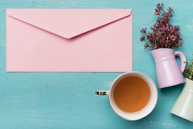 Photo gratuit enveloppe fermée rose avec une tasse de thé et vase sur un fond en bois bleu