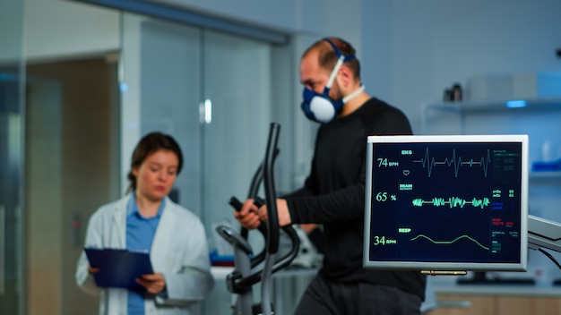 Photo gratuit équipe de chercheurs en médecine surveillant la vo2 des sports de performance masculins portant un masque en cours d'exécution. docteur en sciences de laboratoire mesurant l'endurance d'un sportif pendant que l'analyse ekg s'exécute sur un écran d'ordinateur en laboratoire