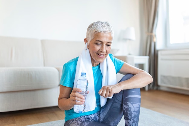 Photo gratuite femme âgée tenant une bouteille en plastique de sueur essuyant avec une serviette épuisée après l'entraînement quotidien